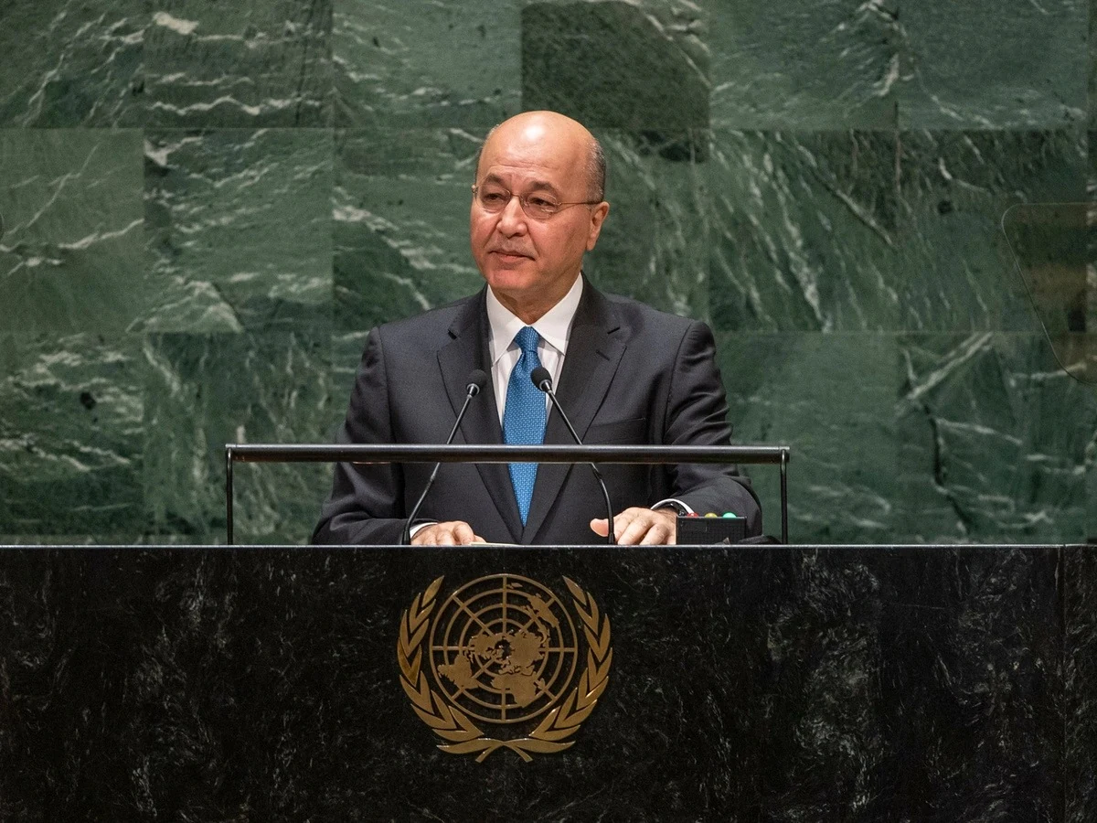 A man gestures while speaking behind a desk