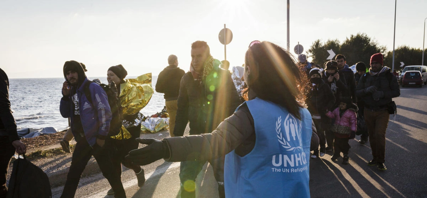 UNHCR staff member directs a group of refugees toward a bus