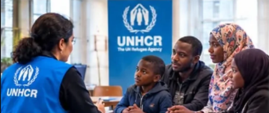 A UNHCR staff member in a blue vest talks with a refugee family at a desk